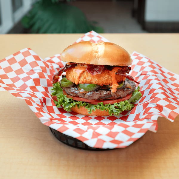 Fred's Burger with bacon, onion ring, jalapeños, lettuce, and tomato on a red checkered paper.