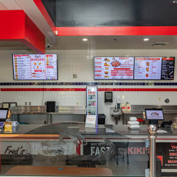 Fred's Burger restaurant interior with menu boards, a counter, and a "Pick Up Here" sign.