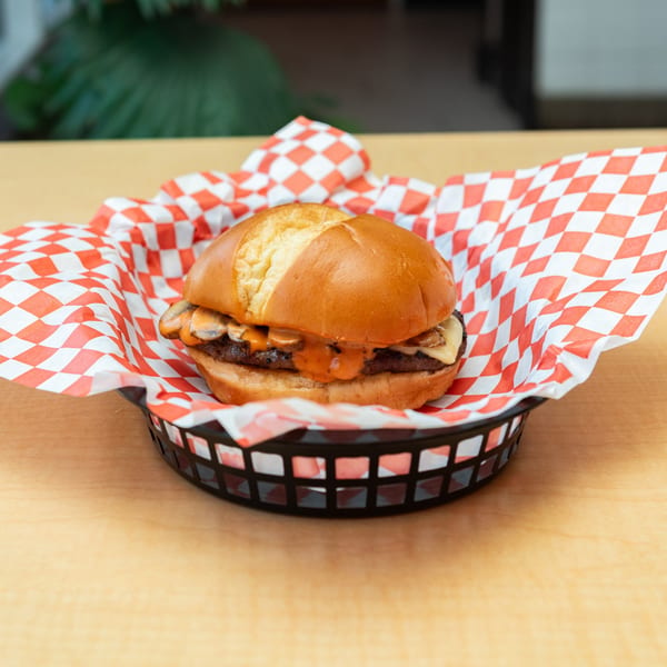 Fred's Burger with mushrooms and melted cheese, served in a basket with red and white checkered paper.