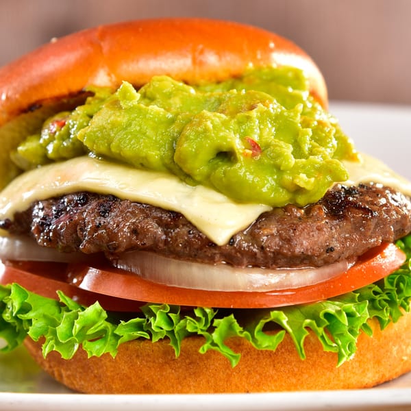 Fred's Burger with a thick patty, melted cheese, guacamole, tomato, onion, and lettuce on a bun.