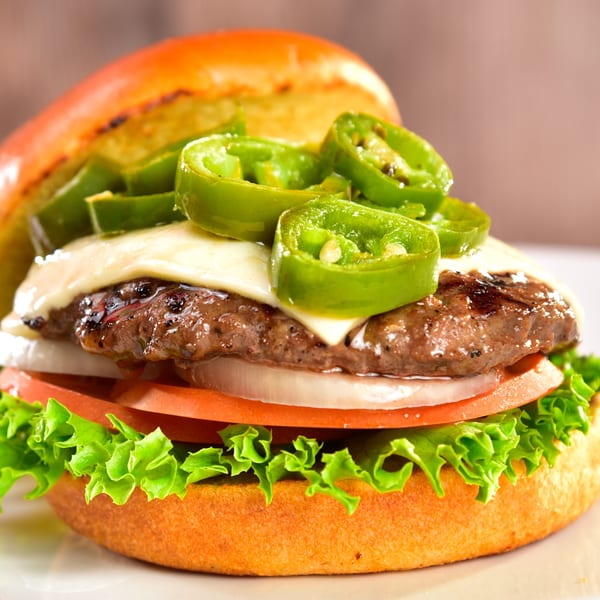 Fred's Burger with melted cheese, sliced jalapeños, onions, tomatoes, and lettuce on a bun.