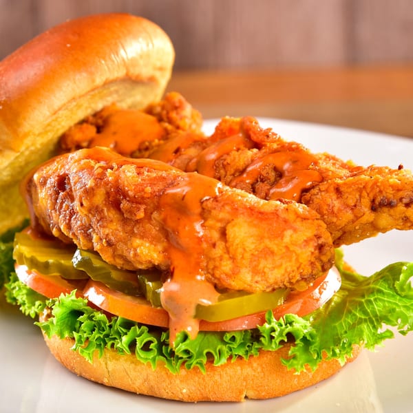 Fred's Burger fried chicken sandwich with sauce, lettuce, tomato, and pickles on a bun.