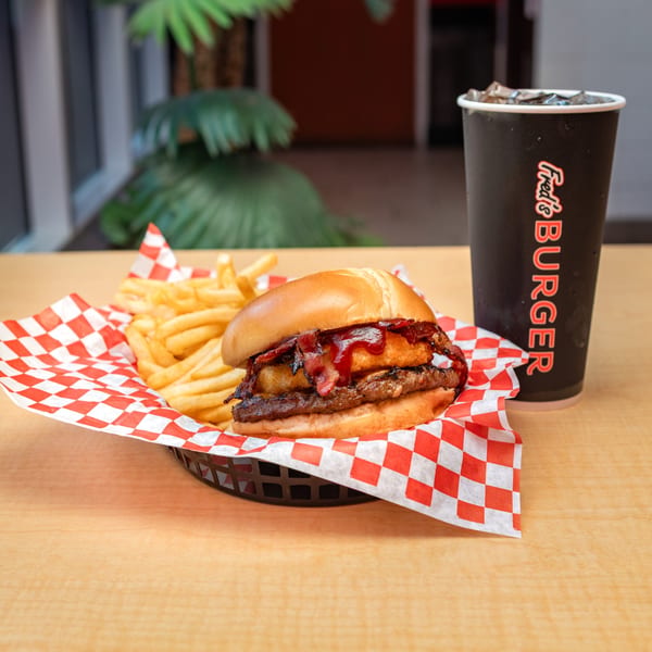 Fred's Burger with bacon, onion rings, and BBQ sauce, served with fries and a drink.