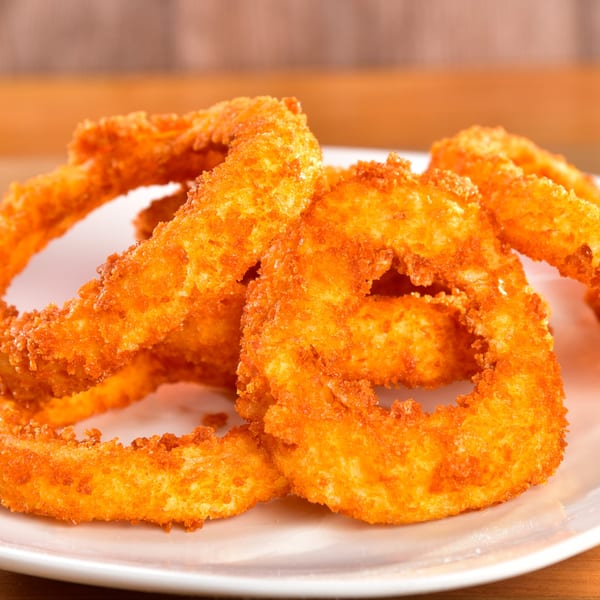 Close-up of golden-brown, crispy onion rings piled on a white plate at Fred's Burger.