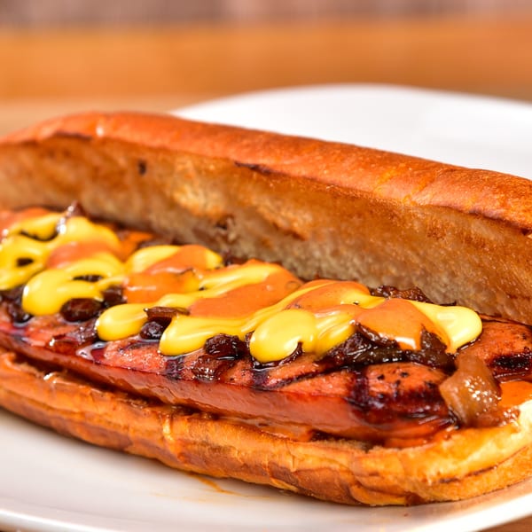 Fred's Burger hot dog with mustard, ketchup, and caramelized onions on a white plate.