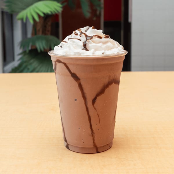 Fred's Burger chocolate milkshake with whipped cream and chocolate drizzle on a light wooden table.