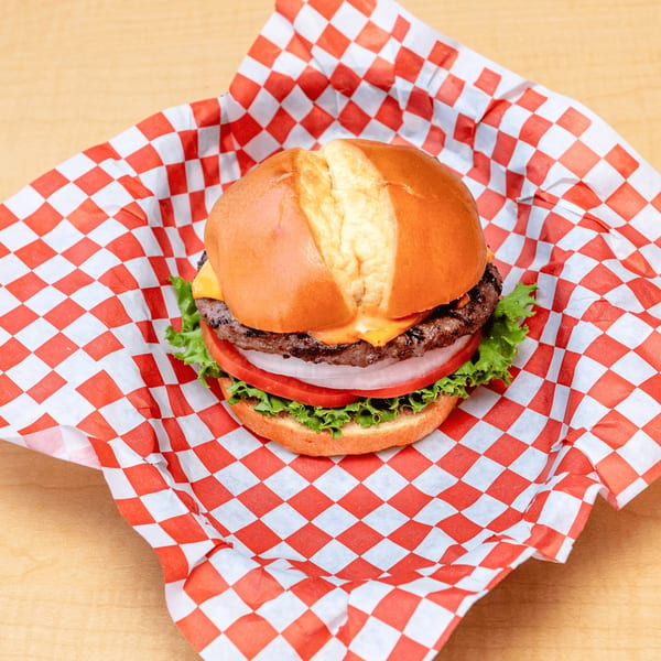 Fred's Burger with cheese, lettuce, tomato, and onion, served in red and white checkered paper.