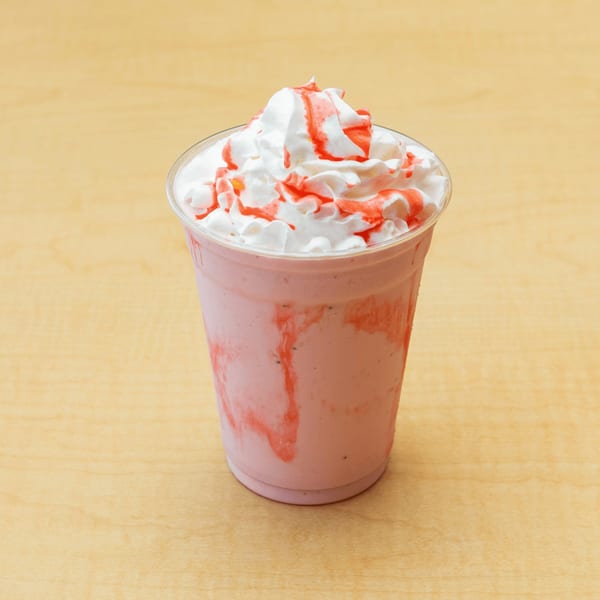 Fred's Burger strawberry milkshake with whipped cream and strawberry syrup on a wooden table.