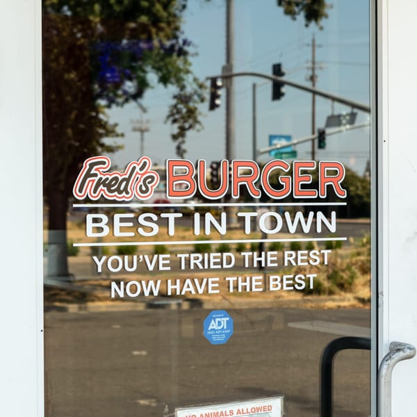 Fred's Burger restaurant entrance door with "Best in Town" slogan and street reflections.
