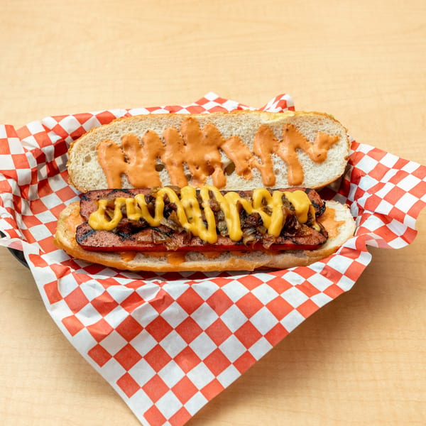 Fred's Burger hot dog with mustard and grilled onions in a red and white checkered basket.