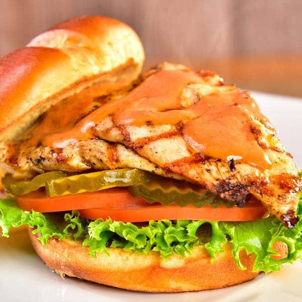 Fred's Burger grilled chicken sandwich with sauce, pickles, tomato, and lettuce on a bun.