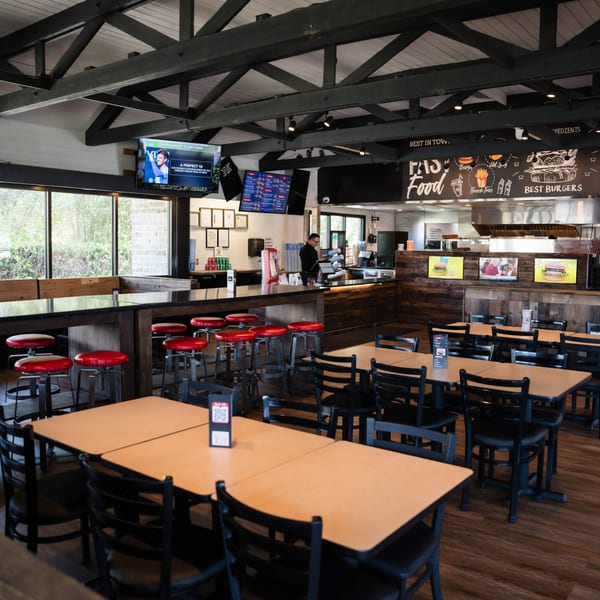 Interior of Fred's Burger restaurant with tables, red bar stools, and a counter with an employee.