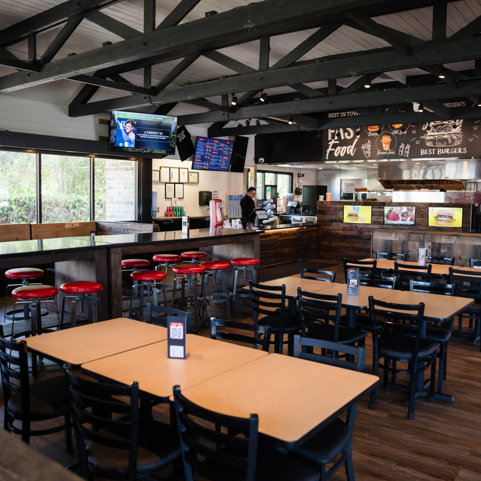 Interior of Fred's Burger restaurant with tables, red bar stools, and a counter with an employee.
