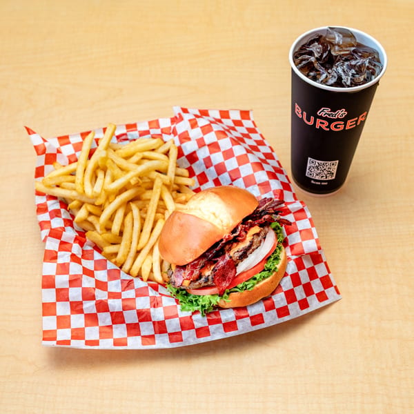 Fred's Burger bacon cheeseburger with fries in a red checkered basket and a soda.